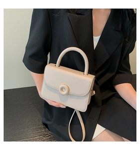 Beige PU leather handbag with gold clasp held by a model in a black blazer
