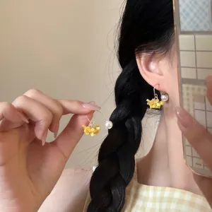 Close-up of floral tassel earrings with yellow flowers and white pearl on a gold hook