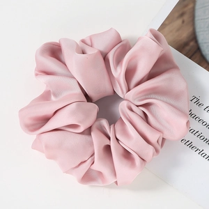 Close-up of soft pink satin oversized scrunchie with elegant pleated texture and silky shine