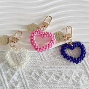 Detail of handmade beaded heart-shaped keychains in white, pink and purple with gold clasps