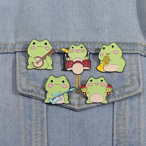 Detailed view of five cartoon frog musician enamel pins on a light blue denim jacket pocket