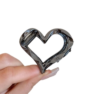 Handheld view of a hollow heart-shaped metal hair claw clip in shiny gun black finish