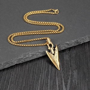 Close-up of golden arrowhead pendant on a venetian chain over black wood background