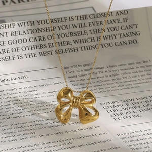 Detailed view of a gold bow-shaped pendant necklace on a vintage newspaper background