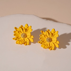 Close-up of yellow floral stud earrings with 3D petals on a beige textured surface