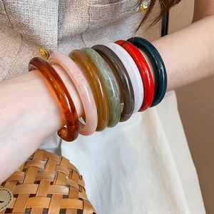 Close-up of a model wearing eight colorful resin bangles with a vintage marble texture