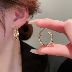 Boucles d'oreilles créoles torsadées dorées avec zircons, vue rapprochée sur modèle réel