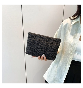 Chic black quilted puff clutch with floral bubble texture held against a soft green shirt