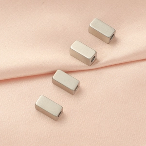 Polished silver cuboid spacer beads for DIY jewelry displayed on soft pink silk fabric