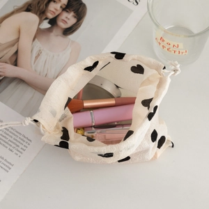 Detail view of champagne drawstring pouch with black hearts showing cosmetics inside