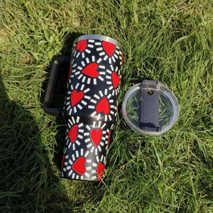 Detail of 40oz black tumbler with red heart pattern and clear lid on green grass