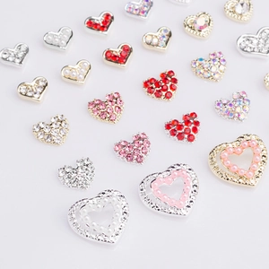 Detailed view of 3D heart nail charms with rhinestones and pearls on white background