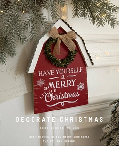 Close-up of red wooden Christmas house sign with green wreath and burlap bow on pine branch