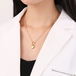 Detailed close-up of a 3D gold heart pendant necklace worn by a model in a white blazer