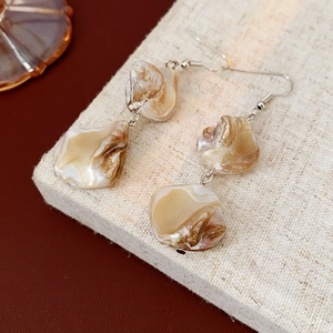 Détail de boucles d'oreilles pendantes en nacre marron irrégulière avec crochets argentés