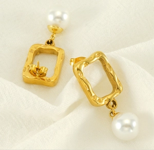 Detail of gold hammered rectangular frames and white pearls on a textured fabric base