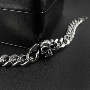 Polished stainless steel Cuban chain bracelet with 3D skull detail on black leather background