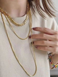 Close-up of layered gold Cuban link and flat snake chains on a beige knit sweater
