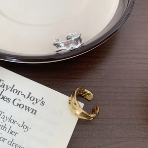 Detail of gold and silver irregular S925 rings with green stones on a wooden background