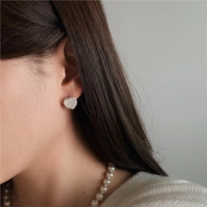 Close-up of heart-shaped shell stud earring worn by model on a neutral gray background