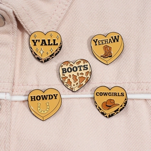 Close-up of Western cowboy heart enamel pins with cow print on a pink denim jacket