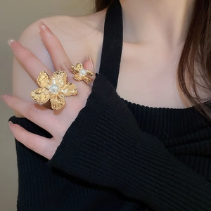 Detailed view of irregular gold flower rings with pearls worn on fingers against black fabric