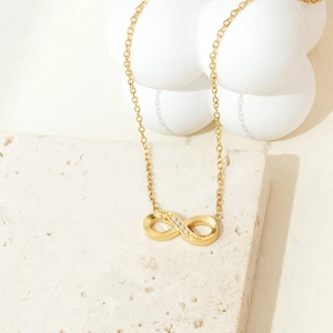 Detailed close-up of golden infinity necklace with zircon accents on travertine stone