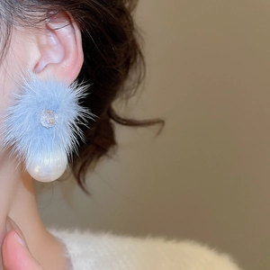 Detail view of a 18K gold-plated earring with blue fur pom-pom, pearl, and zircon