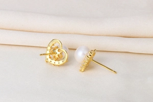 Detail of gold heart earrings with white pearl and sparkling zircon on silk background