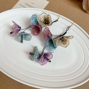 Detail of fabric flower tassel earrings with blue and purple mesh petals on white plate