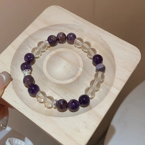 Macro detail of natural amethyst and quartz bead bracelet on a premium wooden display tray