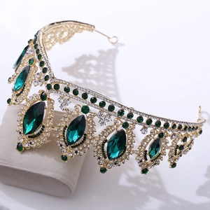 Golden baroque bridal crown with emerald green crystals on a beige display pillow