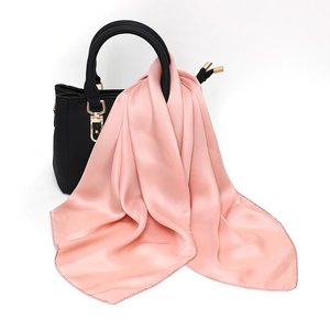 Close-up of a pink satin square scarf draped elegantly on a textured black leather handbag
