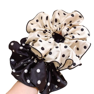 Elegant polka dot satin scrunchies in black and white worn on a wrist against white background