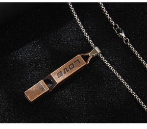 Macro shot of bronze whistle pendant with LOVE engraving and silver chain necklace