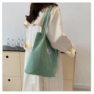 Close-up of green corduroy tote bag showing soft texture and crossbody strap on model
