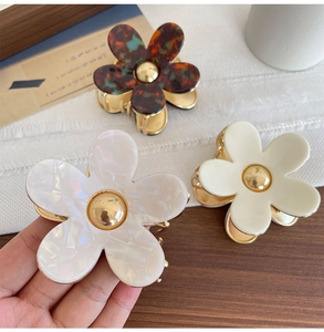 Detailed close-up of acetate flower hair claws in cream, shell white, and tortoiseshell finish