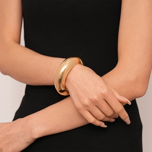 Polished gold wide cuff bracelet styled on model wrist with minimalist metal design