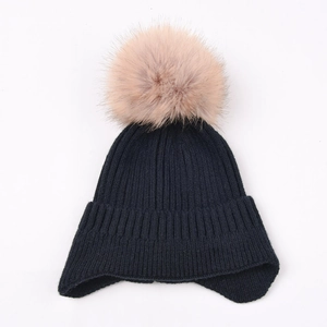 Close-up of navy blue knit earflap hat featuring a large soft pink faux fur pom-pom detail