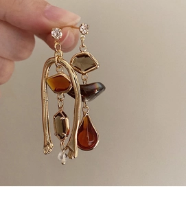 Detail of asymmetric long drop earrings with amber crystals and gold-tone tassels