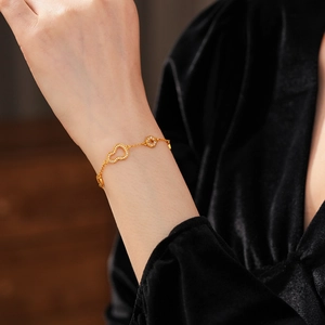 Detailed view of 24k gold-plated bracelet with gourd and coin charms on a wrist