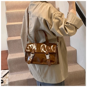 Detail of dark brown glossy messenger bag showing double silver buckles and strap texture