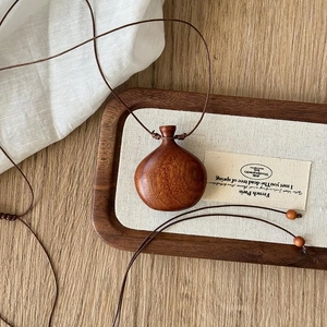 Close-up of wood bottle pendant on linen fabric with vintage braided wax cord necklace