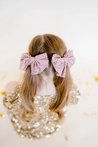 Detail of pink embroidered lace bow hair ties on a girl's pigtails with gold accents