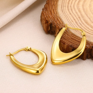 Detail of gold U-shaped hoop earrings with a polished mirror finish on a beige background