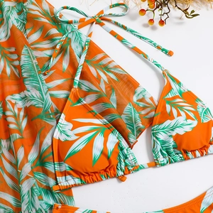 Flat lay of orange tropical print three-piece bikini set with sheer mesh sarong cover-up