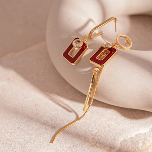 Asymmetric gold geometric earrings with red resin, rhinestone accents, and long chain tassels