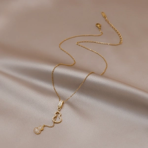 Détail du collier gourde dorée avec design ajouré et pendentif pompon en zircon brillant