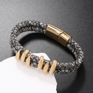 Macro shot of grey-black braided leather bracelet with golden magnetic clasp and textured rings