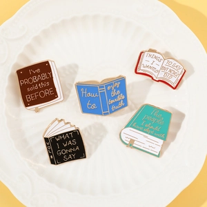 Detailed view of five colorful enamel book pins with creative quotes on a white plate